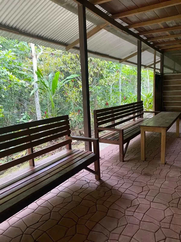 Covered outdoor sitting area in a jungle retreat with wooden benches and a table, surround
