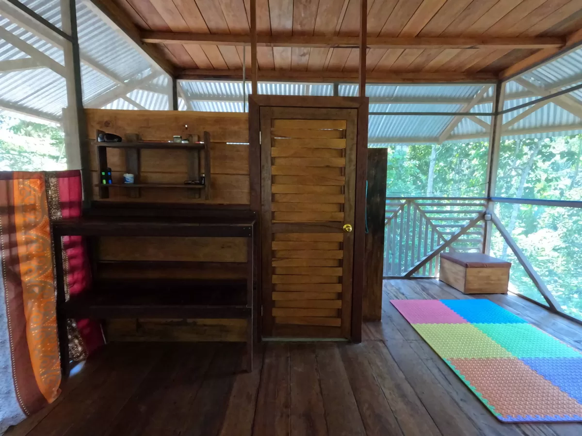 Innenansicht eines Holzhauses im peruanischen Dschungel mit Naturblick, Yoga-Matte und Regalen – ideal für Retreats und nachhaltiges Leben