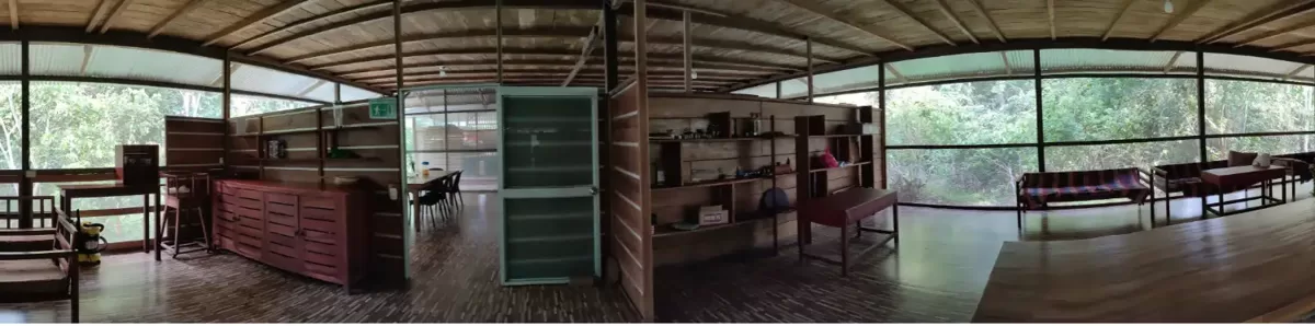 Vista panorámica del interior del área común del eco-lodge, con estanterías, mesas y ventanales a la selva.
