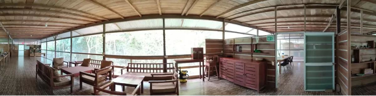 Sala común panorámica del eco-lodge con sofás, mesas de madera, estanterías y vista a la selva.